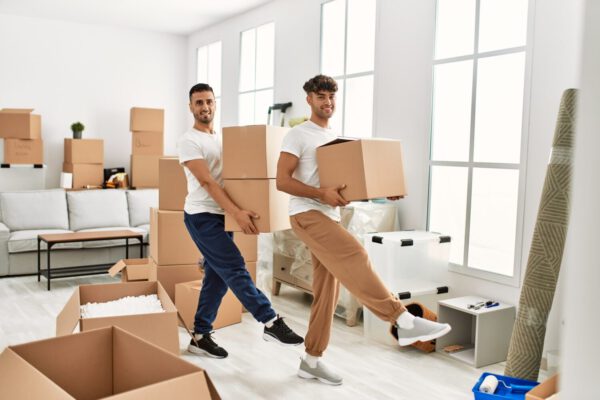 Two hispanic men couple smiling confident holding cardboard boxes at new home